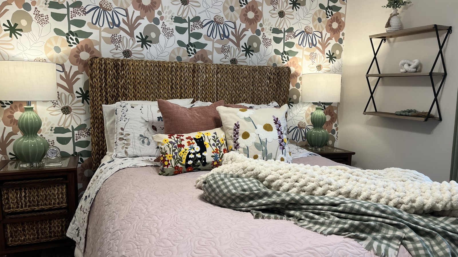A finished bedroom with layered bedding, patterned wallpaper, lamps, and accessories fully styled